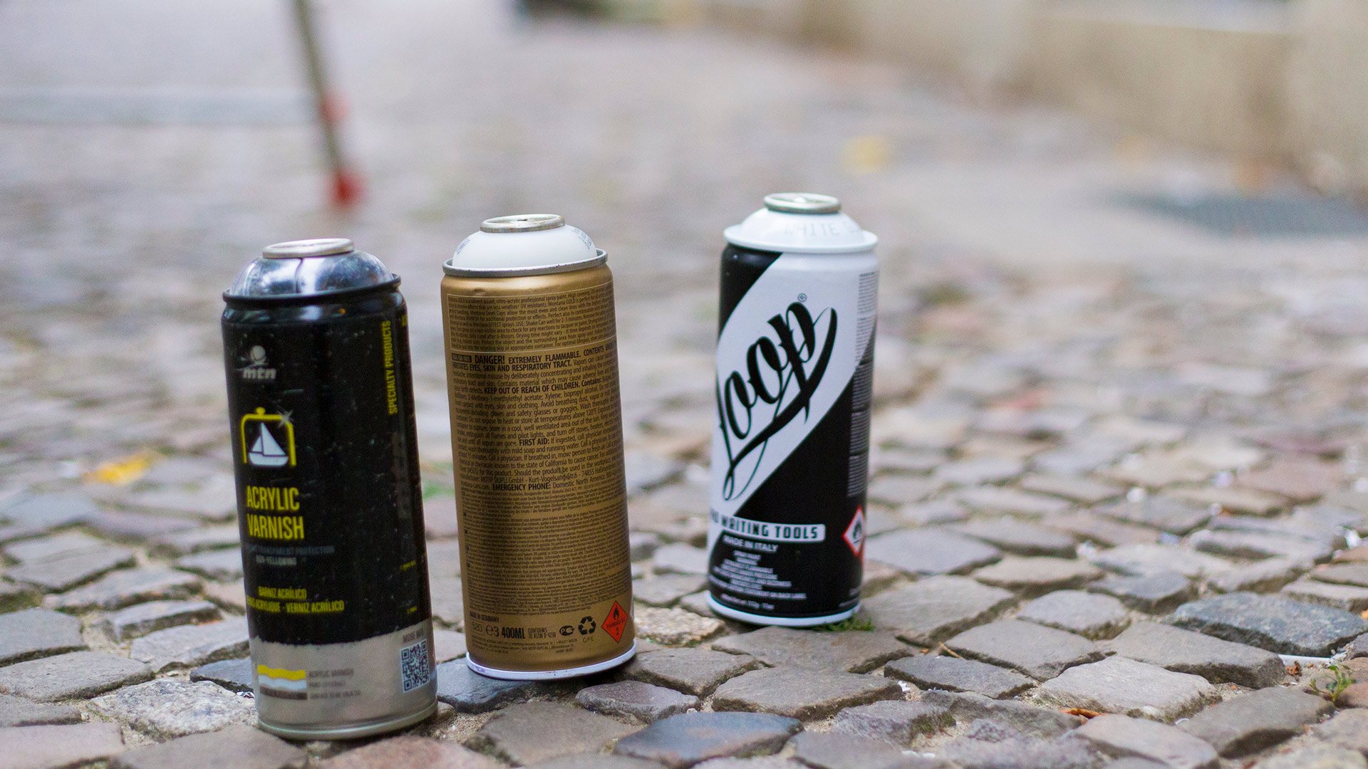 Drei Sprühdosen auf Kopfsteinpflaster